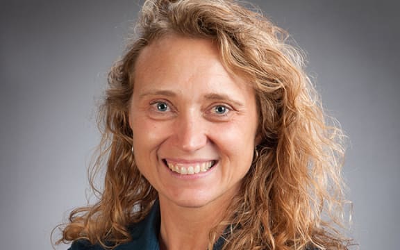 A headshot of a smiling woman with long curly blonde hair