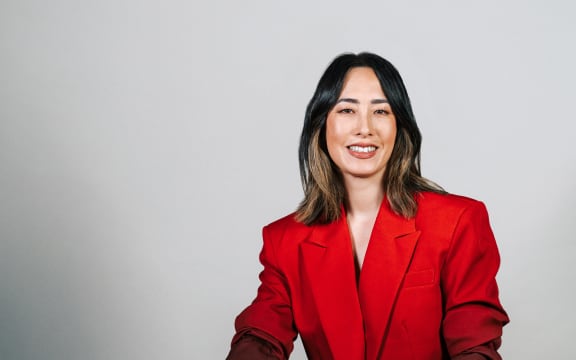 Melissa Leong sits in a red suit in front of a plain white background.