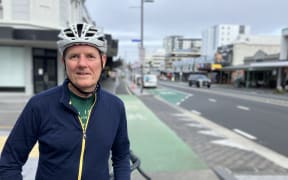 A man, wearing a helmet, standing next to his bike on the Karangahape Road cycleway.