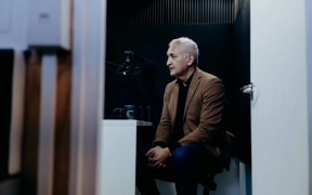 Looking through a doorway to journalist and news reader Mike McRoberts in recording studio.