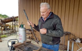Allan Birchfield winnows the tiny gold flakes on a piece of paper to shake any dirt out; the flakes are smelted in a ceramic pot (crucible) in a small gas-fired furnace.