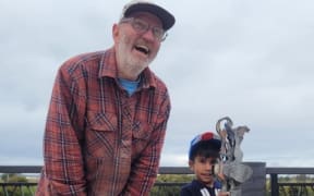 Sculptor Jeff Thomson presents a corrugated iron trophy to the winner of the 2024 Kaipara River paper boat race.