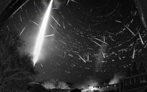 A black-and-white wide-field image of the night sky showing a bright white streak from top to bottom of image. Smaller streaks are visible too.