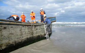 Japanese coast guard officers inspect a battered wooden boat where eight bodies were found inside at a beach in Oga, in Japan's Akita prefecture.
