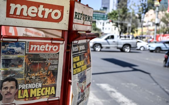 The front page of a local newspaper displays news about the death of Nemesio Oseguera, alias "El Mencho," Mexico's most wanted drug lord in recent years, in Mexico City on February 23, 2026. Mexico has deployed 10,000 troops to quell clashes sparked by the killing of the country's most wanted drug lord, which have left dozens dead, officials said on February 23. Nemesio "El Mencho" Oseguera, leader of the Jalisco New Generation Cartel (CJNG), was wounded on February 22 in a shootout with soldiers in the town of Tapalpa in Jalisco state and died while being flown to Mexico City, the army said. (Photo by Yuri CORTEZ / AFP)