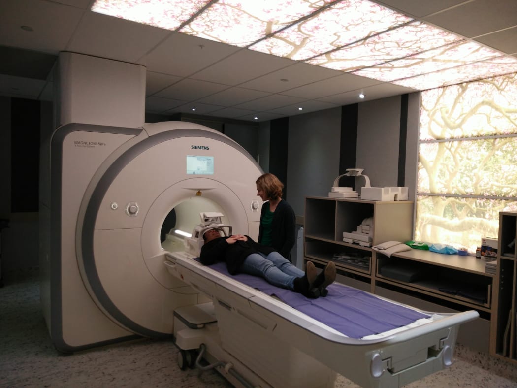 Senior Lecturer Dr Catherine Theys of the University of Canterbury stands next to a study participant in an fMRI scanner.