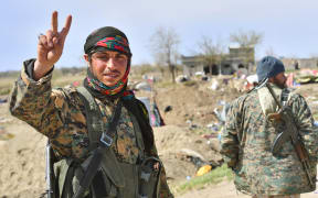 A picture taken on March 23, 2019 shows a fighter of the US-backed Kurdish-led Syrian Democratic Forces (SDF) flashing the V for victory sign in the fallen Islamic State group's last bastion in the eastern Syrian village of Baghuz after defeating the jihadist group.