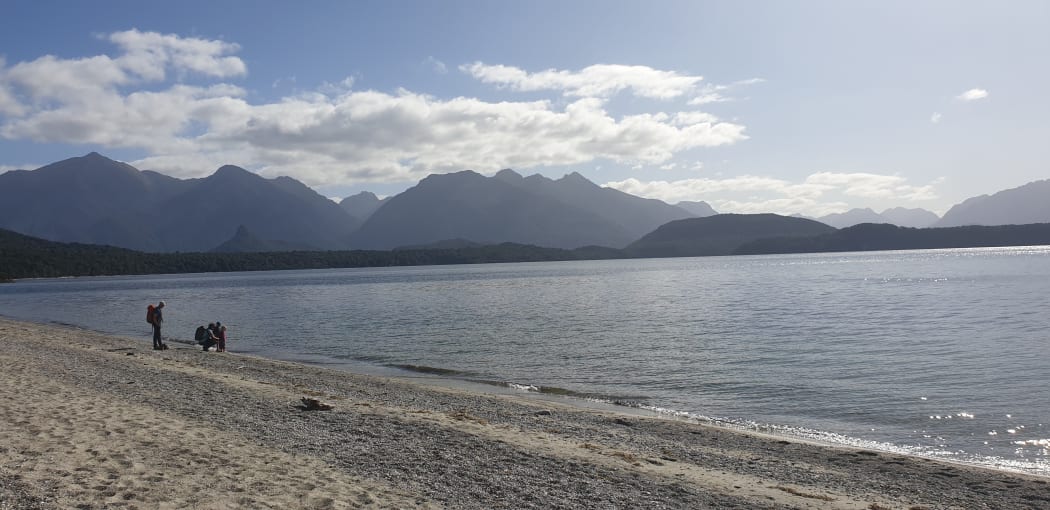 People walk along the shore of Lake Manapouri.