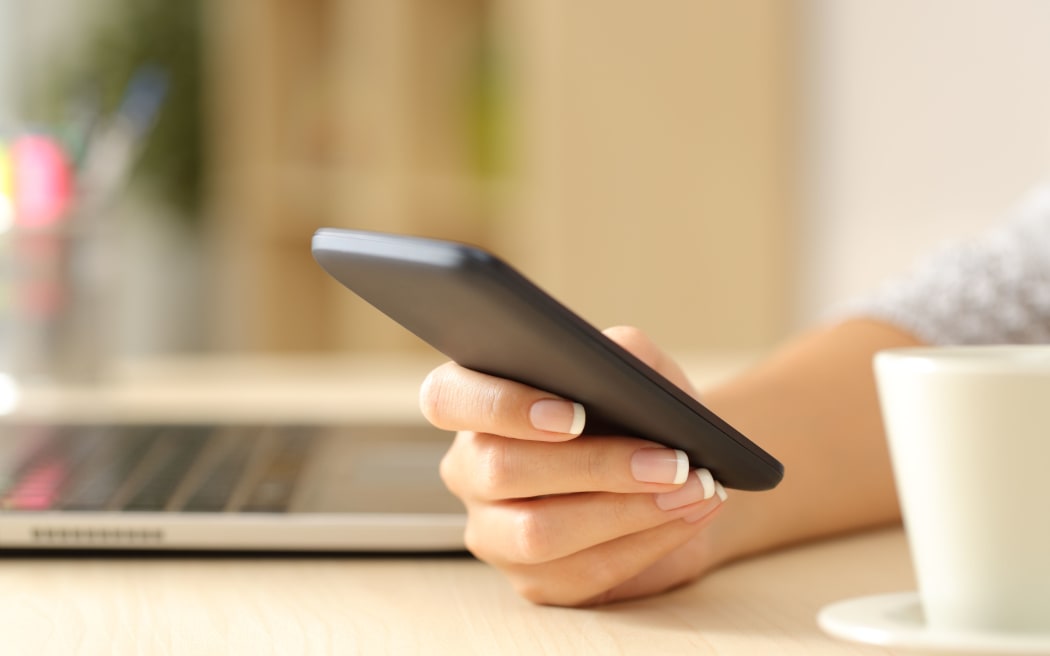 Close up of a woman hand using a smart phone on a desk at home