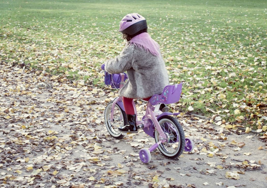 Little girl riding bicycle in autumn landscape, rear view (Photo by Anne-Sophie Bost / AltoPress / PhotoAlto via AFP)