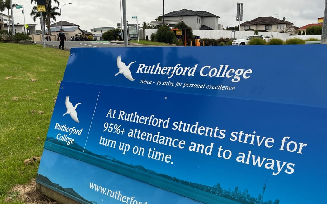 A blue sign near Rutherford College in Te Atatū, Auckland, with school branding on it. The sign says: "At Rutherford students strive for 95%+ attendance and to always turn up on time."