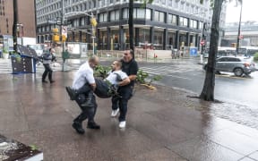 Co-workers carry injured maintenance worker by downed by strong wind tree after tropical storm Isaias lashes out New York City.