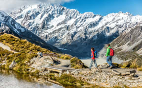Hiking travel nature hikers in New Zealand mountains. Couple people walking on Sealy Tarns hike trail route with Mount Cook landscape, famous tourist attraction.