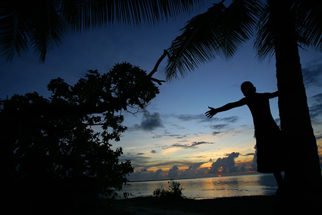 A child on Kiribati watches the sunset on an ever rising ocean.