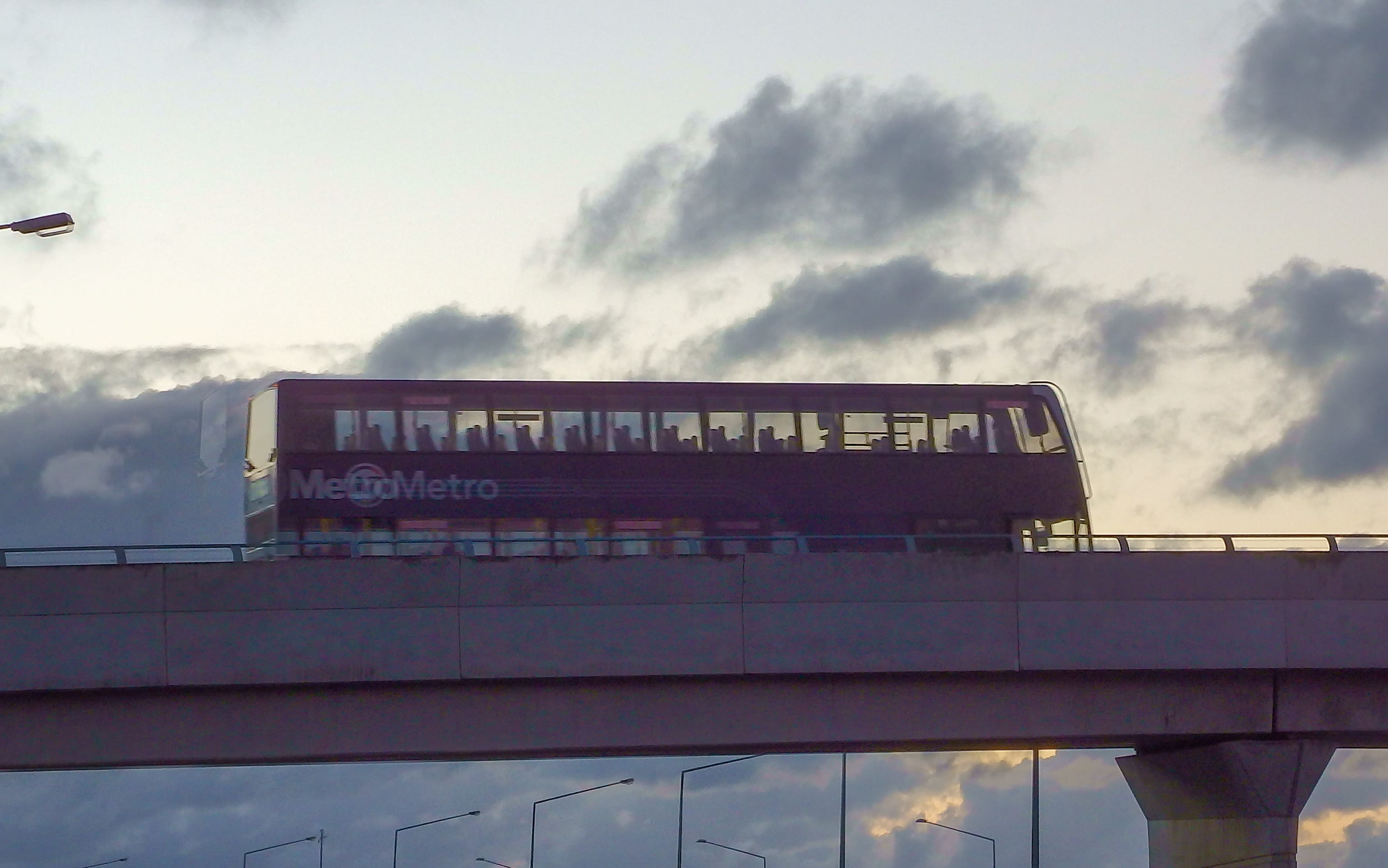 Double decker bus goes on a flyover against a back lit sky in Auckland New Zealand.