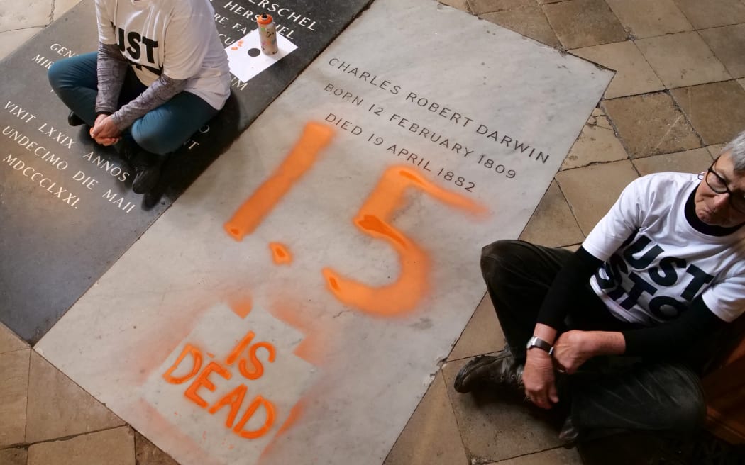 A handout picture taken and released by the Just Stop Oil climate campaign group on January 13, 2025, shows two activists, sitting on the floor alongside the grave of Charles Darwin, after they sprayed "1.5 is dead" over it in protest against climate change in action, inside Westminster Abbey in central London. Activists Alyson Lee and Di Bligh from the Just Stop Oil group on Monday painted inscriptions on the grave of famous naturalist Charles Darwin in to protest against political inaction on global warming. In a video posted by the group on X, two activists were seen writing in orange paint "1.5 is dead", a reference to the 1.5°C limit on global warming set by the international Paris climate agreement. (Photo by JAMIE LOWE / Just Stop Oil / AFP) / RESTRICTED TO EDITORIAL USE - MANDATORY CREDIT "AFP PHOTO /  JUST STOP OIL / JAMIE LOWE " - NO MARKETING - NO ADVERTISING CAMPAIGNS - DISTRIBUTED AS A SERVICE TO CLIENTS