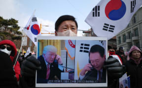 A supporter of impeached South Korean president Yoon Suk Yeol holds a placard of Yoon (R) and incoming US president Donald Trump (L) that translates as “He responded by sending his special regards to the people of South Korea”, during a rally near his residence in Seoul on January 6, 2025. - South Korean investigators trying to arrest suspended President Yoon Suk Yeol have asked for an extension to the warrant that expires on January 6, with the embattled leader holed up in his residence. (Photo by Anthony WALLACE / AFP)