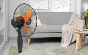Interior of light living room with cozy grey sofa and modern floor fan