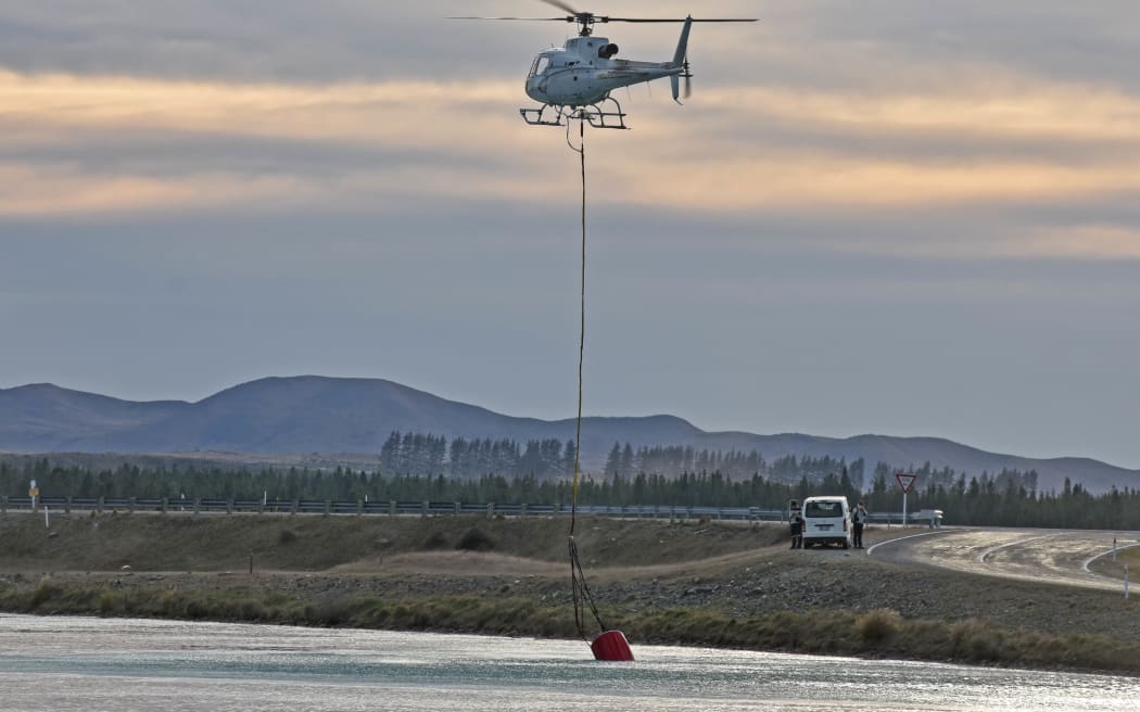 Squirrel helicopter operated by Heliventures, which are based at Pukaki Airport. The helicopter is using a monsoon bucket to pick up water out of the Pukaki Canal just west of State Highway 8.  Photo - Chris Rudge, Red Cat Biplane Flights