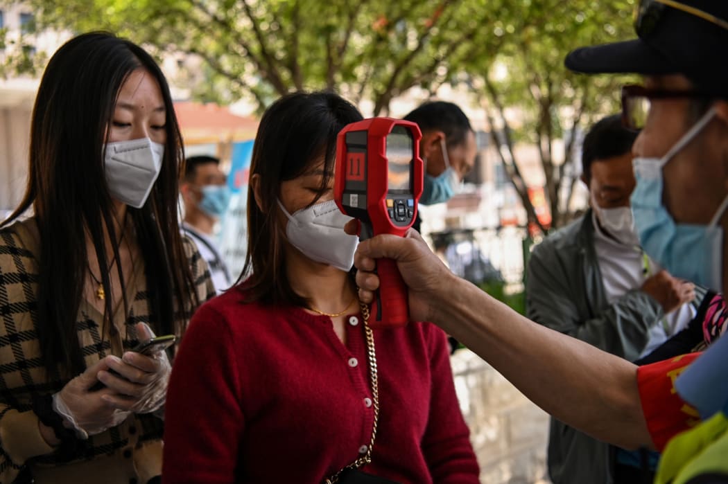 A worker wearing a face mask checks passengers body temperatures and a health code on their phones before they take a taxi after arriving at Hankou railway station in Wuhan, China's central Hubei province on May 12, 2020.