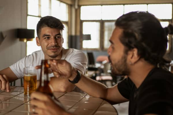 Two men chat at a table with beers.