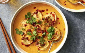 A bowl of red curry soup and dumplings.