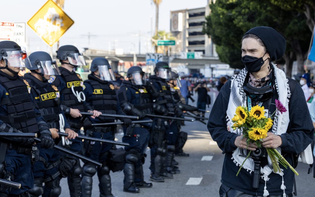 A demonstrator holding flowers walks past police officers as protesters clash with law enforcement in the streets surrounding the federal building during a protest following federal immigration operations in Los Angeles.