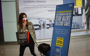 A passenger wearing a face mask as a precaution against the novel coronavirus walks past a sign at Heathrow airport, west London, on May 22, 2020.