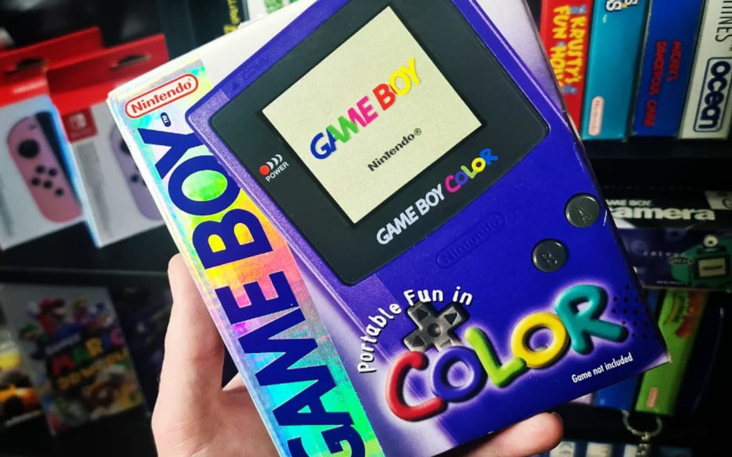 Jarrod's hand holds a box containing a Game Boy colour. In the background are colourful titles of various video games.