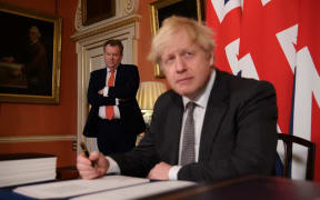 UK chief trade negotiator, David Frost (L) looks on as Britain's Prime Minister Boris Johnson (R) signs the Trade and Cooperation Agreement between the UK and the EU, the Brexit trade deal, at 10 Downing Street in central London on December 30, 2020.