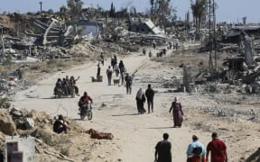 Displaced Palestinians walk past destroyed buildings as they return to their homes in the in al-Zahra area, north of the Nuseirat refugee camp in the central Gaza Strip, on 14 October, 2025, a day after a ceasefire came into effect.