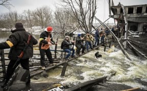 Members of a Ukrainian civil defence unit pass new assault rifles to the opposite side of a blown up bridge on Kyiv's northern front on 1 March, 2022.