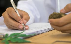 Doctor writing on prescription blank and bottle with medical cannabis on table close up