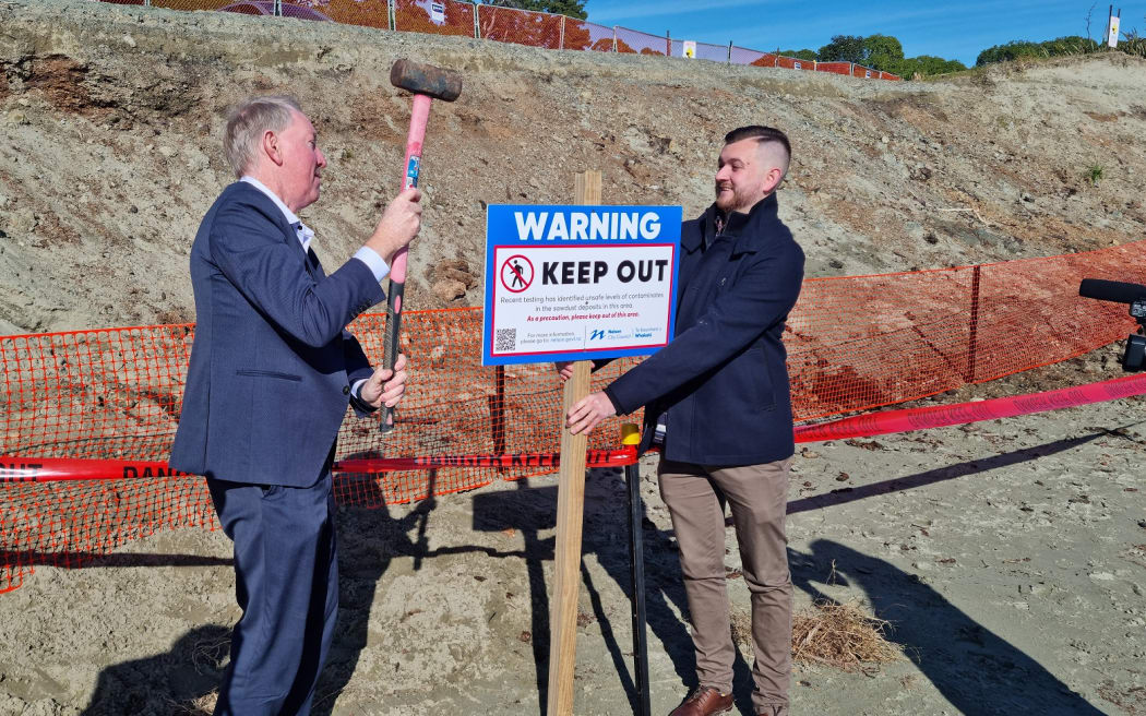 Nelson Mayor Nick Smith and councillor Campbell Rollo erect a sign warning people of contaminated wood waste at Tāhunanui Beach.