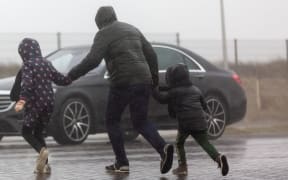 picture of a family who is crossing a street while it is heavy raining