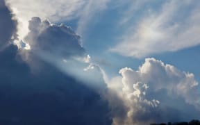 Dark and white clouds with shafts of sunlight and patches of blue sky.