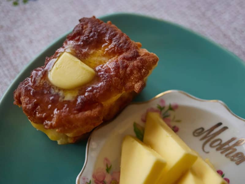 A mini loaf of fry bread is buttered and sitting on a green plate.