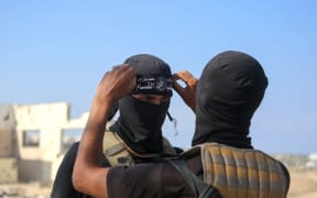 A Palestinian militant fighter of the Ezzedine al-Qassam Brigades, the armed wing of the Palestinian Hamas movement, fixes the headband of the group on his comrade's forehead as vehicles of the International Committee of the Red Cross (ICRC) (not pictured) transport the second batch of released Israeli hostages in the south of Deir el-Balah in the central Gaza Strip, on October 13, 2025. (Photo by Bashar TALEB / AFP)