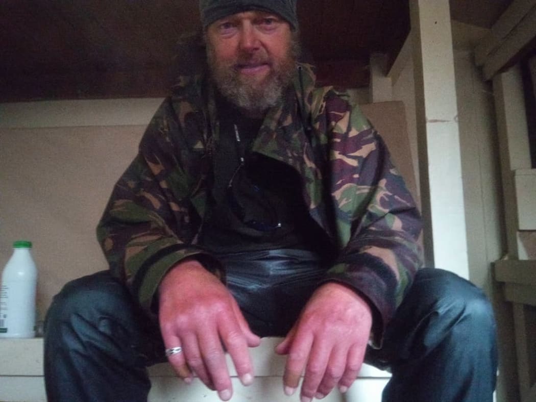 A portrait of a rain-sodden Bruce Hopkins sitting on the edge of a bunk in a mountain hut.