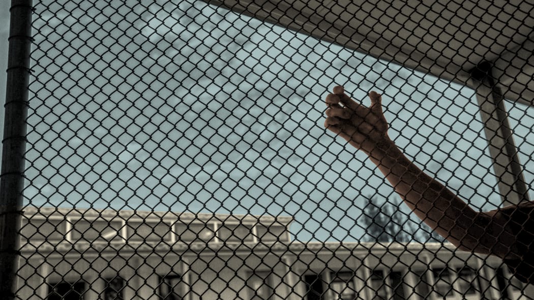 A hand holds onto the wire in prison