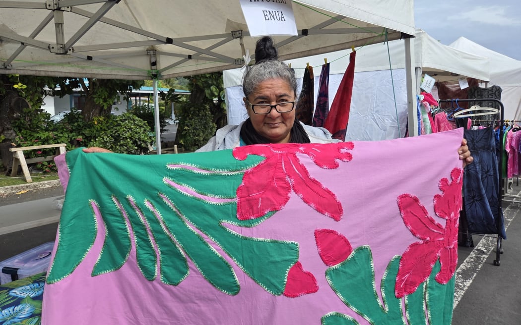 Koi Bishop from Aitutaki holding up a double bed spread, selling at the market on behalf of a Mama who needed to go to New Zealand for medical treatment.