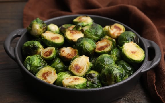 Delicious roasted Brussels sprouts in baking dish on wooden table, closeup.