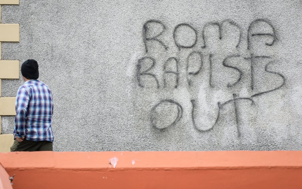A pedestrian walks past a graffiti reading "Roma rapists out" after a second night of an anti-immigration demonstration in Ballymena, Northern Ireland, on June 11, 2025. Police in Northern Ireland on June 11 condemned "disgraceful" scenes of violence on a town's streets after a second night of rioting targeting foreigners in which 17 officers were injured. The unrest was triggered following the arrest of two teenagers accused of attempting to rape a young girl. The youngsters appeared in court on Jube 9 where they asked for a Romanian interpreter. (Photo by PAUL FAITH / AFP)