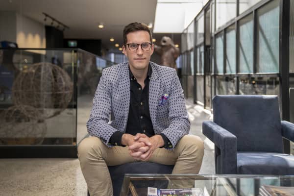 Ed McKnight is a smartly dressed man with glasses sitting with his legs apart on a stool.