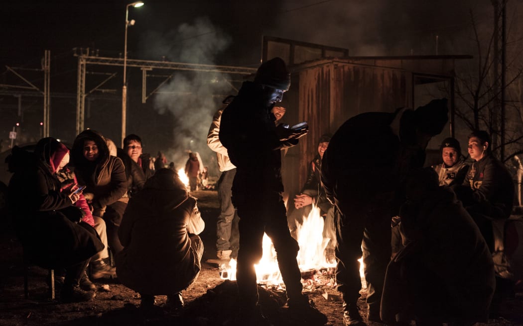 Migrants and refugees try to keep warm by a fire as they wait for a train after crossing the Macedonian border into Serbia on January 29, 2016 near the town of Presevo.