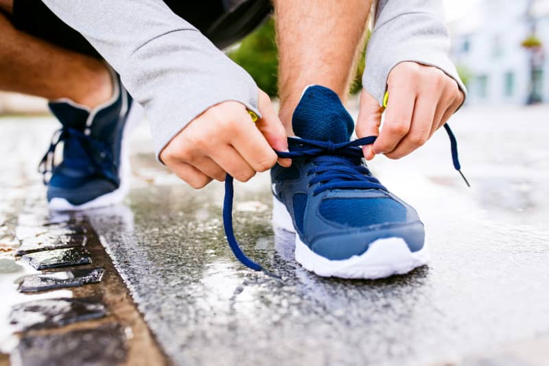A person crouching on wet outdoors tying their shoe laces.