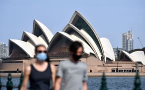 People wearing face masks walk in front of the Opera House in Sydney, New South Wales.