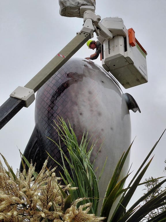 Sculptor Phil Price up in a cherry picker, inspecting where a lifting hook will make contact with the Rakaia salmon statue to remove it for renovation.