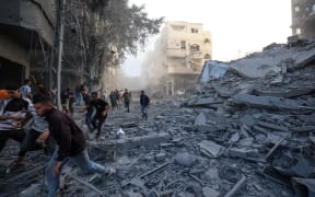 People run for cover following an Israeli strike that targeted a building in the Bureij camp for Palestinian refugees in the central Gaza Strip on October 19, 2025. Gaza's civil defence agency said a series of Israeli air strikes on October 19 killed at least 11 people across the territory, as Israel and Hamas traded blame for violating a ceasefire. (Photo by Eyad BABA / AFP)