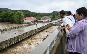 People check on high waters in a flood-affected area after heavy rains above a bridge at Xin'anzhuang village, in Miyun district, on the outskirts of Beijing on July 28, 2025. A landslide triggered by unusually heavy rain killed four people and left eight others missing in northern China's Hebei province, state media said on July 28, as downpours force thousands to evacuate. (Photo by Jade GAO / AFP)